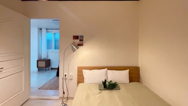 A bedroom with a bed, a bedside lamp, and a view into another room. - House Lotus (Seoul)