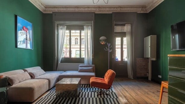 Ein Wohnzimmer mit Sofa, Sessel und Couchtisch, Holzboden und einer grünen Wand.