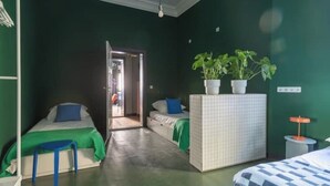Ein Zimmer mit zwei Betten, einem kleinen Tisch, einer Topfpflanze und einer Tür zu einem weiteren Raum.