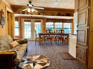 A cozy room with a wooden ceiling, a dining table with chairs, a couch, and a patterned rug. - Turman's Slice of Heaven: Lake Fork water front cabin (Yantis)