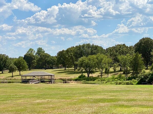 A grassy field with a wooden pavilion, trees, and a clear sky. - Turman's Slice of Heaven: Lake Fork water front cabin (Yantis)