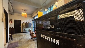 A reception area with a black reception desk labeled "RECEPTION," a wooden chair, and a small table with a vase. - BNK89 Hostel (Bangkok)