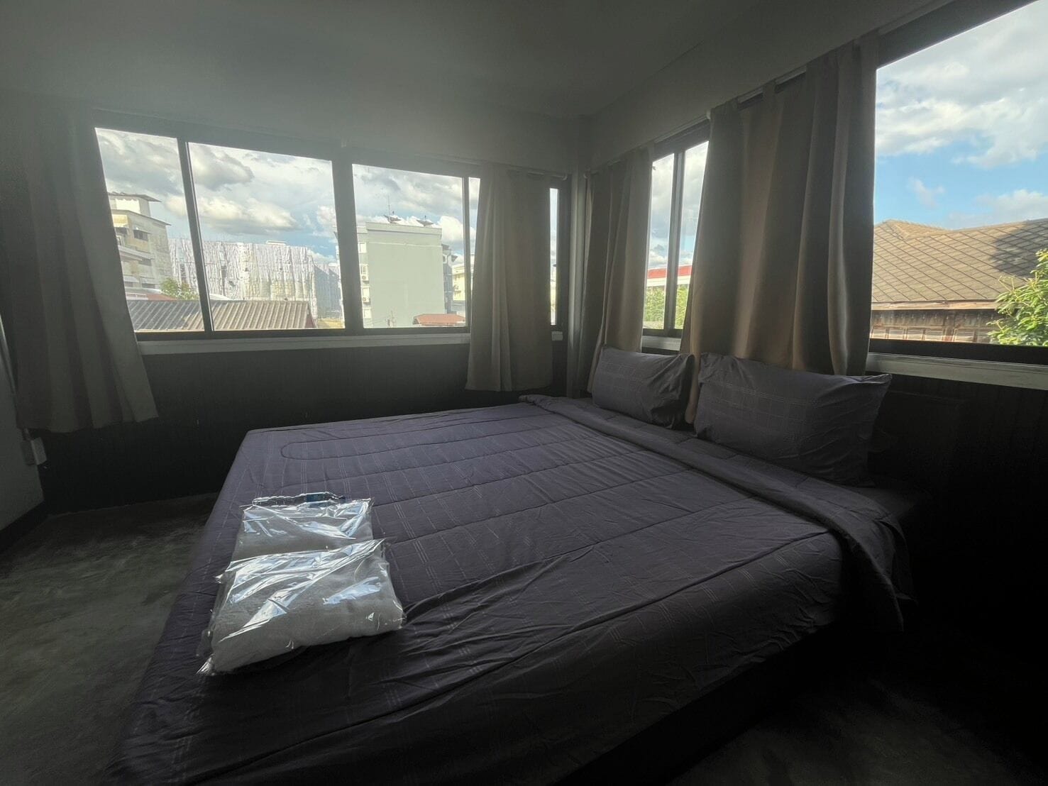 A hotel room with a large bed, a window with curtains, and a view of buildings outside.