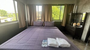 A hotel room with a large bed, two pillows, a water bottle, and towels. There is a dresser with a mirror and a small cabinet with decorative items. - BNK89 Hostel (Bangkok)