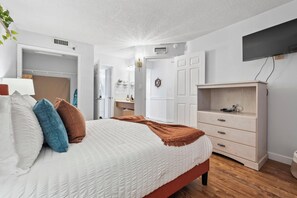 Een slaapkamer met een bed, een dressoir, een televisie en een deur naar de badkamer.