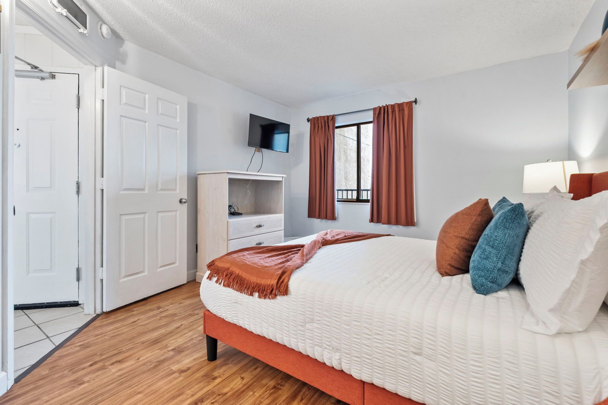 Une chambre à coucher avec un lit, une télévision, une armoire et une fenêtre avec des rideaux.