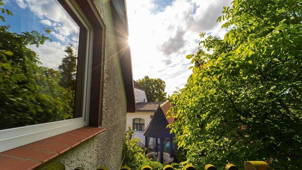 A view through a window with a stone wall, a wooden fence, and lush greenery. - Vacation apartment Cantnitz, your retreat in the middle of the Feldberg lake district. (Feldberger Seenlandschaft)