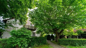 A stone building with a wooden balcony, surrounded by lush greenery and a cobblestone path. - Vacation apartment Cantnitz, your retreat in the middle of the Feldberg lake district. (Feldberger Seenlandschaft)