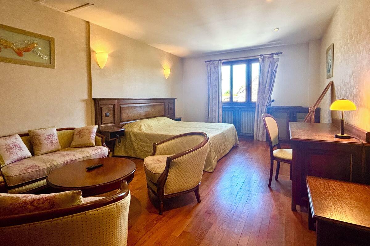 A hotel room with a bed, a sofa, a chair, a small table, and a desk with a lamp.