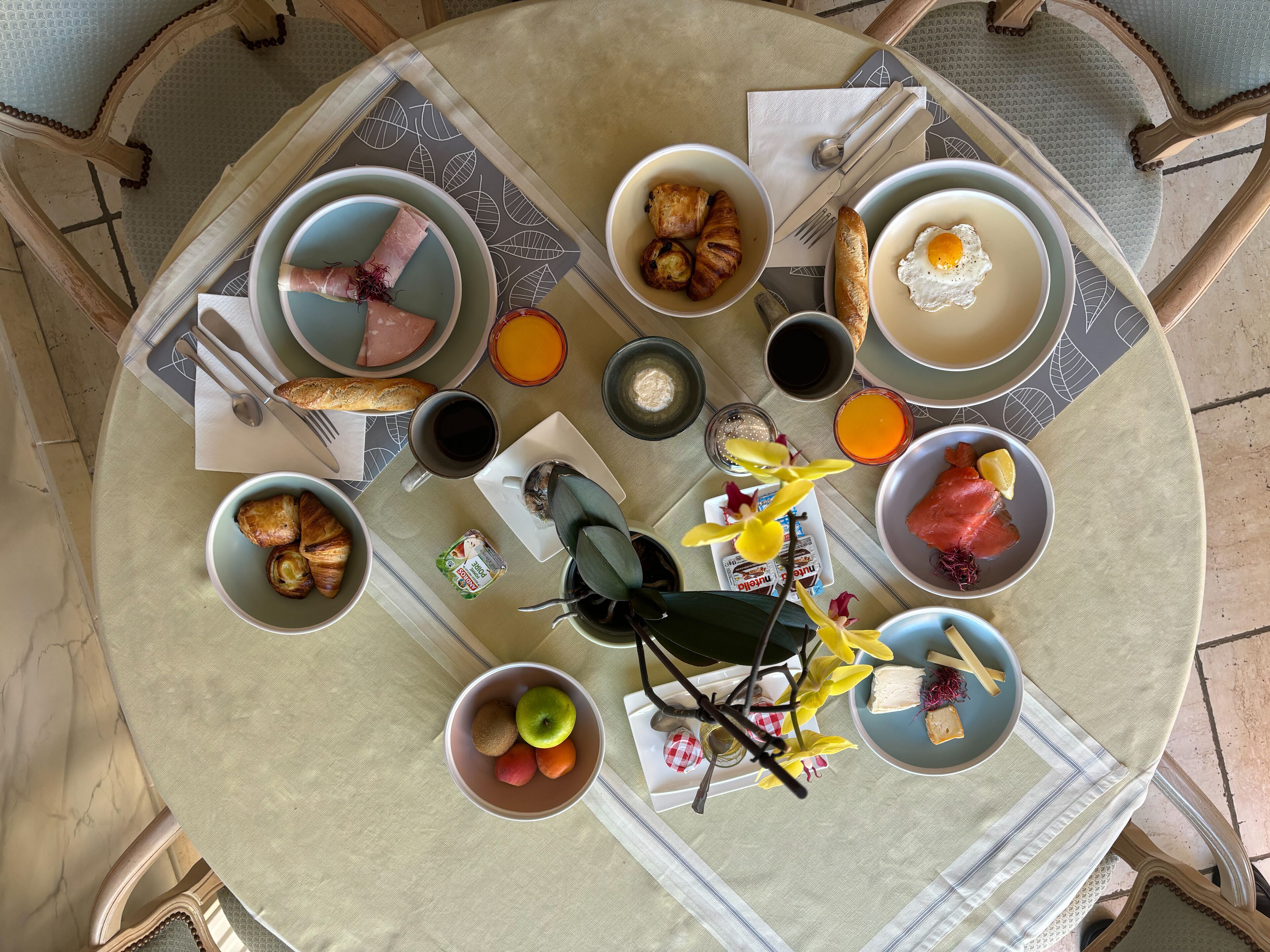 A breakfast setting with various dishes, including croissants, eggs, and fruits, arranged on a table with a view of the floor.