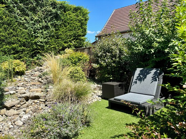 A garden with a stone pathway, a wicker chair, and various plants. - Hôtel Losset (Flagey-Echézeaux)