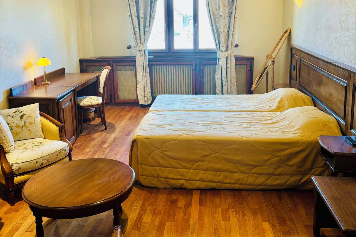 A hotel room with a bed, two chairs, a desk, a lamp, and a window with curtains.