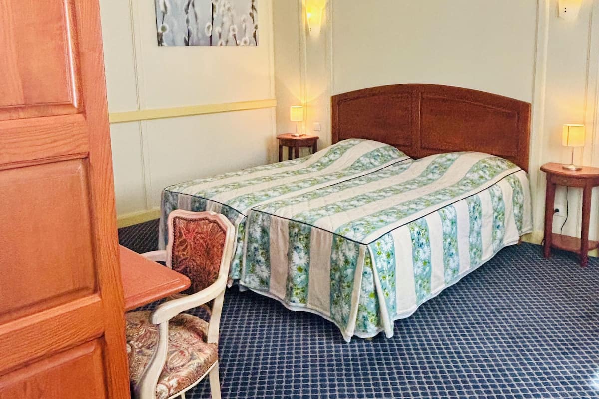 A hotel room with a bed, a chair, a small table, and a wall-mounted artwork.