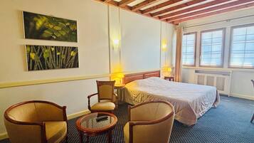 A hotel room with a bed, two armchairs, a small table, a lamp, and artwork on the wall.