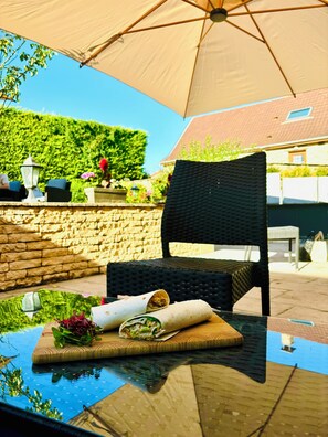 An outdoor seating area with a wicker chair, a glass table, and a large umbrella. - Hôtel Losset (Flagey-Echézeaux)