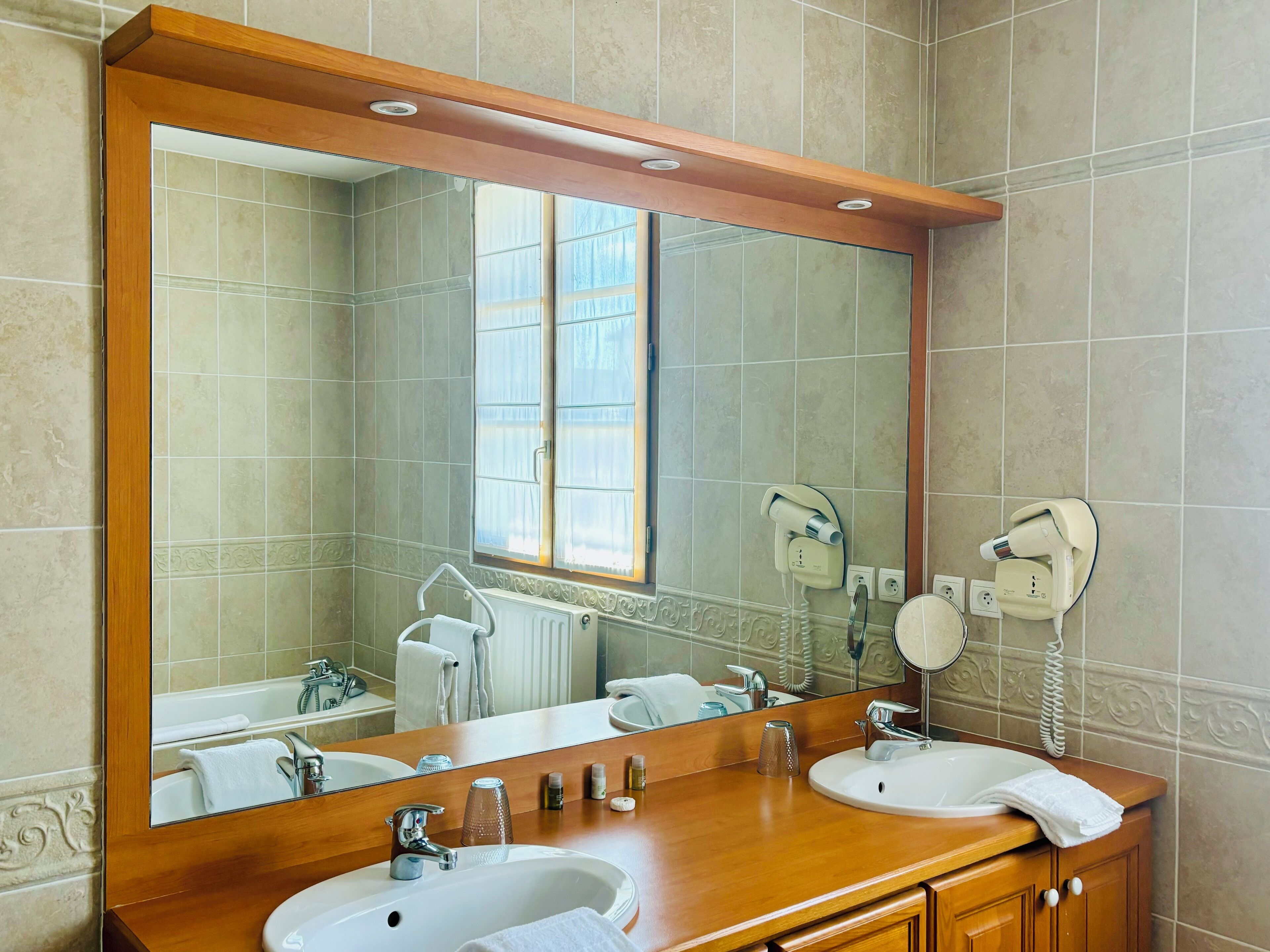 Een badkamer met twee wastafels, een grote spiegel en haardroger bevestigd aan de muur.