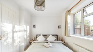 Un dormitorio ordenado con cama, lámparas de noche, un radiador y una ventana con vistas.