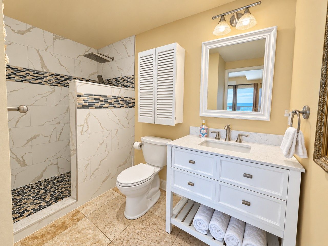 A bathroom with a shower, toilet, vanity, and a large mirror.