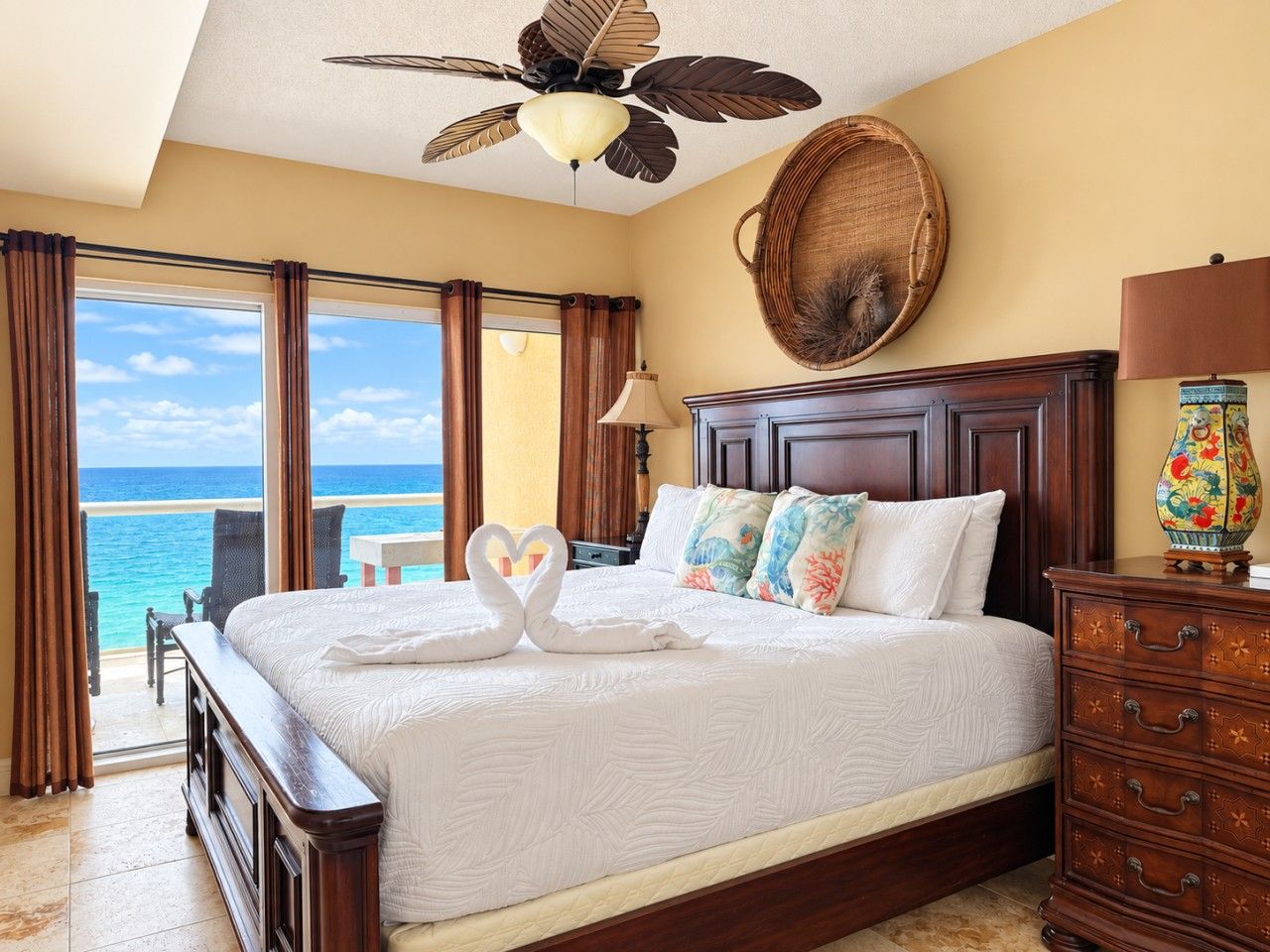 A hotel room with a bed, a wooden dresser, a decorative wall piece, and a view of the ocean.