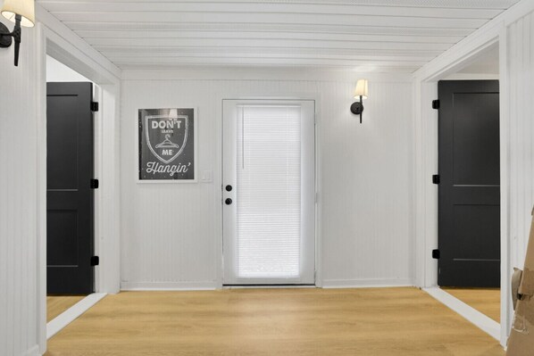 A hallway with white walls, a wooden floor, and a door with a window. There is a sign on the wall that reads "DON'T LEAVE ME HANGIN'". - Millersport: The Summit (Millersport)