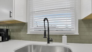 A kitchen with a stainless steel sink, a black faucet, and a window with white blinds. - Millersport: The Summit (Millersport)