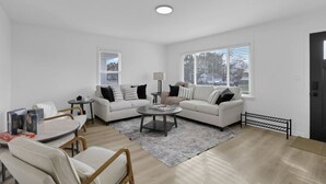 A modern living room with a white sofa, two armchairs, a coffee table, and a small side table. There are books on the side table, and a window with blinds. - Millersport: The Summit (Millersport)