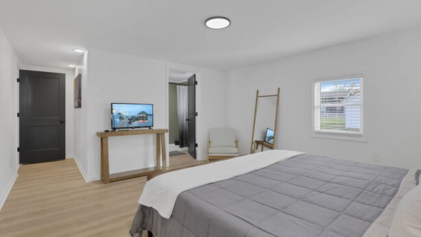A modern bedroom with a bed, a TV on a wooden stand, a chair, and a window with blinds. - Millersport: The Summit (Millersport)