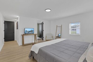 A modern bedroom with a bed, a TV on a wooden stand, a chair, and a window with blinds. - Millersport: The Summit (Millersport)