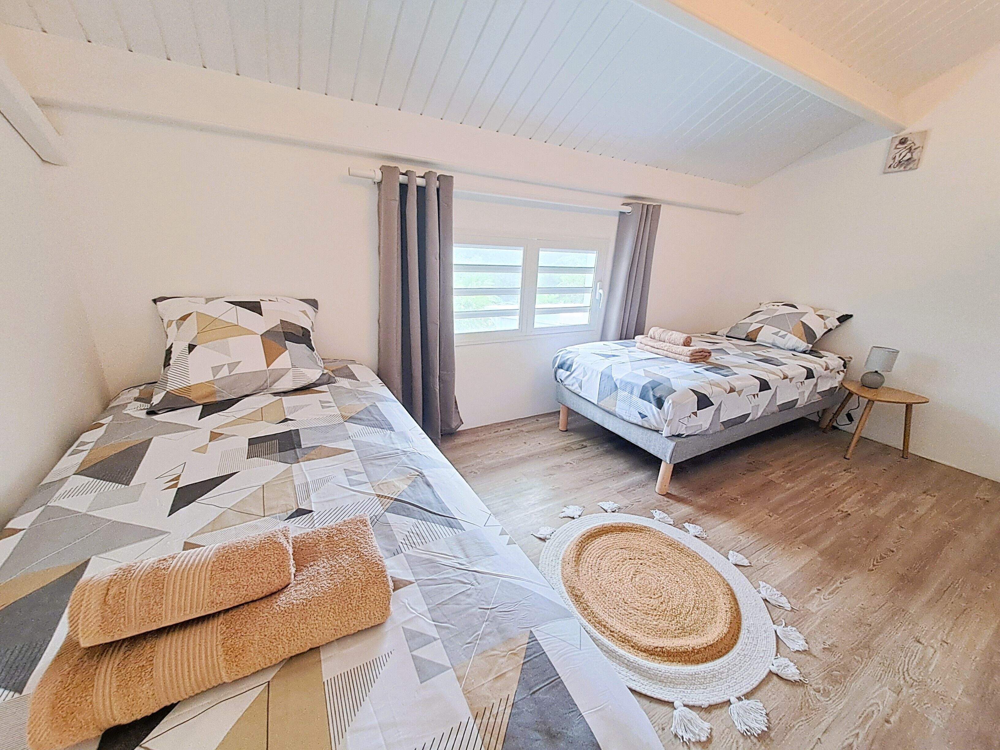 Quarto com duas camas, uma mesinha, janela com cortinas e um tapete tecido no chão.