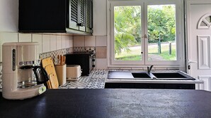 Et køkken med sort bordplade, kaffemaskine, brødrister og et vindue med udsigt til grønne områder.