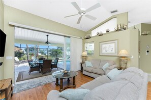 A living room with a glass door leading to a pool area, a ceiling fan, and a sofa with a side table. - Peaceful Oasis, 3-Bedrooms with Saltwater Heated Pool (Rotonda West)