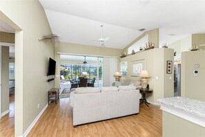 A spacious living room with a large sofa, a dining area with chairs, a ceiling fan, and a view through large sliding doors to an outdoor patio. - Peaceful Oasis, 3-Bedrooms with Saltwater Heated Pool (Rotonda West)