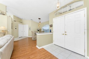 A spacious living room with hardwood flooring, a large white door, and a small island with a sink. - Peaceful Oasis, 3-Bedrooms with Saltwater Heated Pool (Rotonda West)