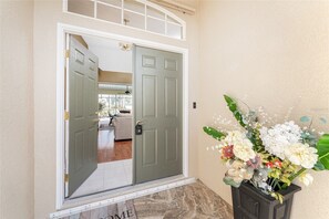 A front door with a glass panel, a small porch area, and a flower arrangement. - Peaceful Oasis, 3-Bedrooms with Saltwater Heated Pool (Rotonda West)
