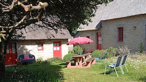 A stone building with a thatched roof, a red door, and a red umbrella in the yard. - Room in thatched cottage in the countryside 2 kms from pointe de la torche (Penmarch)