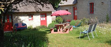 A stone building with a thatched roof, a red door, and a red umbrella in the yard.