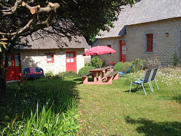A stone building with a thatched roof, a red door, and a red umbrella in the yard. - Room in thatched cottage in the countryside 2 kms from pointe de la torche (Penmarch)