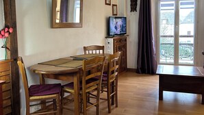 A dining area with a wooden table and chairs, a television, and a view of the outdoors through a door. - 40-square-meter apartment very close to downtown, 40 minutes from Paris Montparnasse (Épernon)