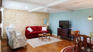 A living room with a red sofa, a patterned armchair, a wooden coffee table, a TV, and a lamp. -  Persimmon Place cozy cabin with AC in Marshall - Perfect for a relaxing getaway (Marshall)
