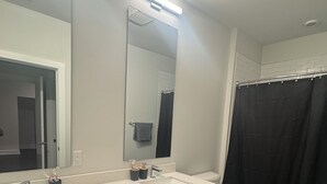 Un bagno moderno con un mobile lavabo in legno scuro, due lavabi, uno specchio grande e una tenda per la doccia.