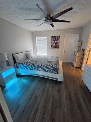 Un dormitorio con una cama, ventilador de techo, ventana con persianas, puerta y cómoda.