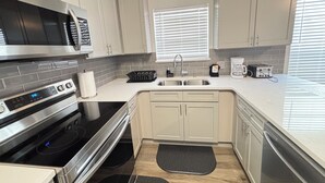 Una cocina moderna con estufa de acero inoxidable, horno integrado, pileta doble y ventana con persianas.