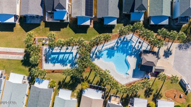 Vista aérea de una zona residencial con piscina rodeada de palmeras y casas con techos inclinados.
