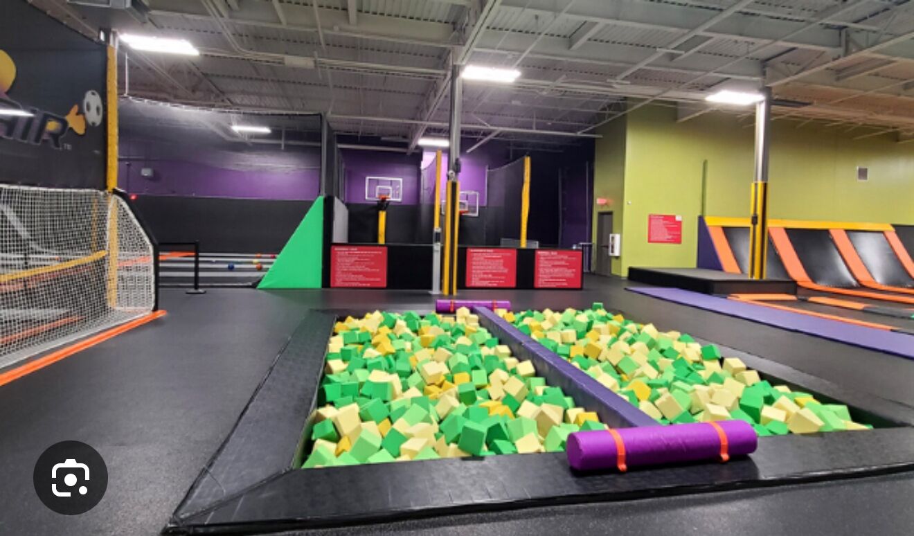 Parque de trampolines cubierto con obstáculos acolchados, zona con red y señalización de seguridad.