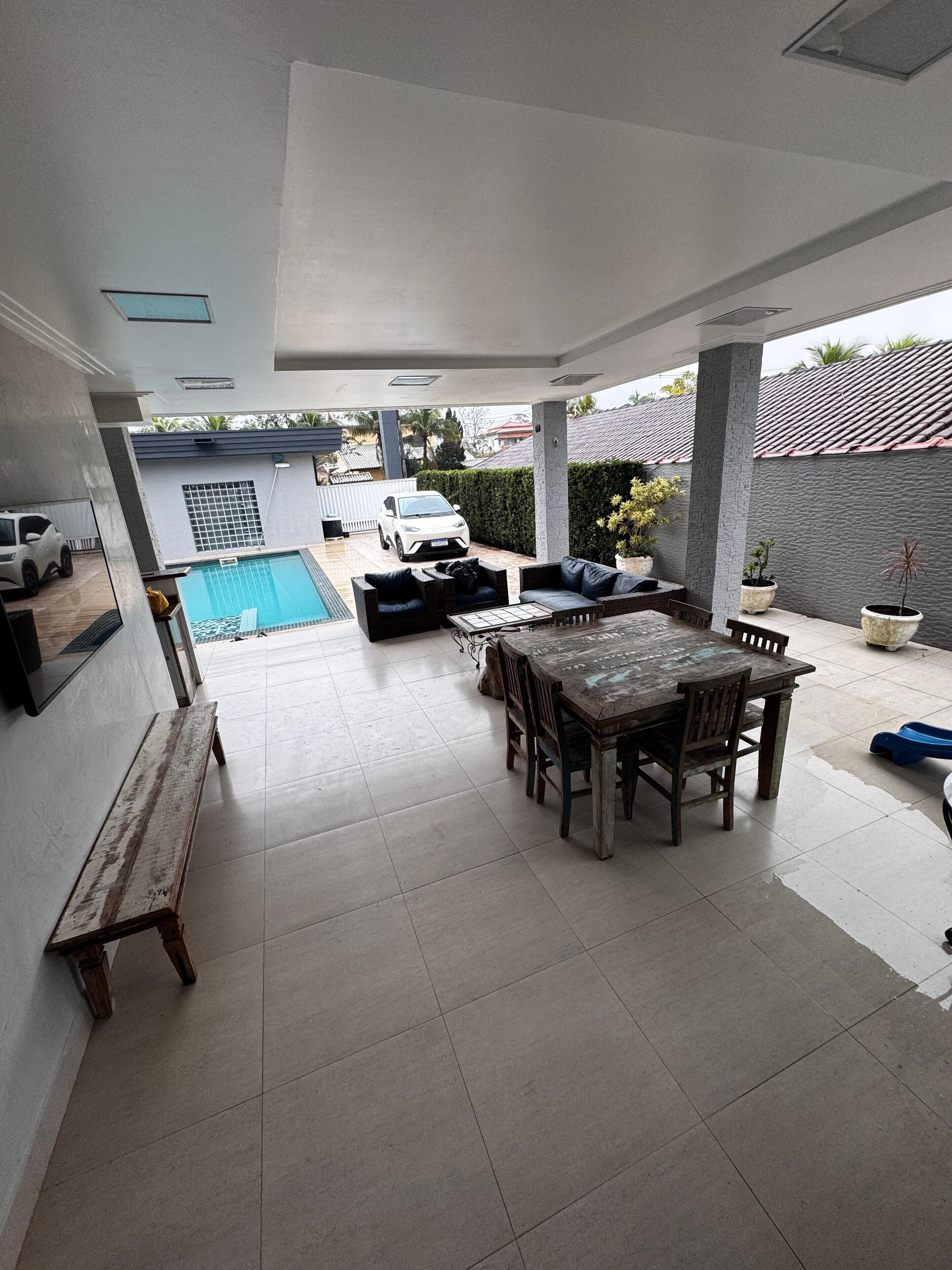A covered patio area with a pool, outdoor seating, and a view of a white car in the background.
