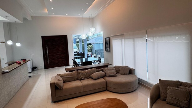 A modern living room with a sectional sofa, a wooden coffee table, and a dining area in the background.