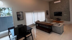 A spacious living area with a dining table and chairs, a sofa, and a TV mounted on the wall.