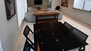 A modern living room with a black dining table, white sofas, and a TV mounted on the wall.