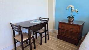 A small room with a wooden table and chairs, a dresser, and a vase with flowers. - 10th Fl Inn on the Park | Pool | AC | City & Park View (Honolulu)