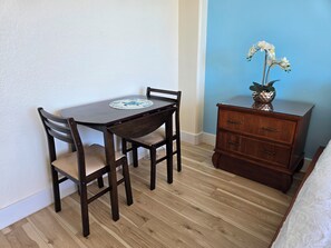 Ein kleines Zimmer mit Holztisch und -stühlen, einem Schminktisch und einer Vase mit Blumen.